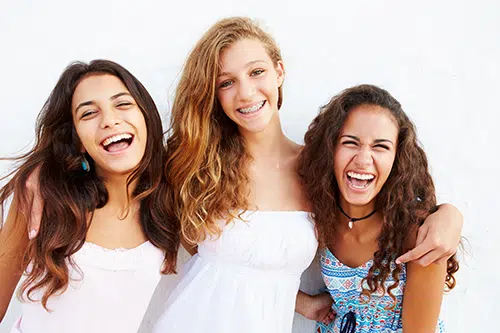 Three teenage girls standing arm in arm and laughing with braces on