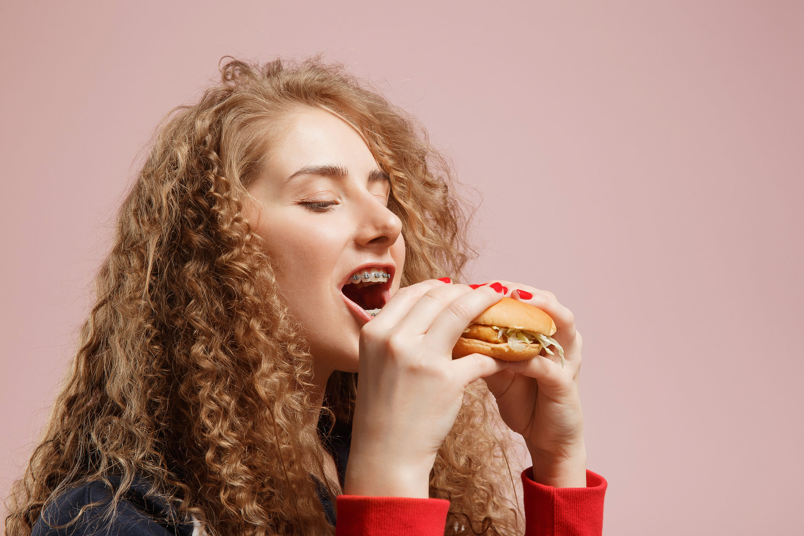 a young lady wearing braces but still enjoying her burger